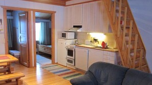 Un espacio habitable compacto con kitchenette, un área de comedor con mesa de madera y un sofá gris.