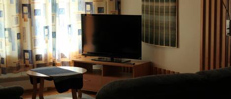 A living room with a flat-screen TV, a wooden desk, and a sofa.