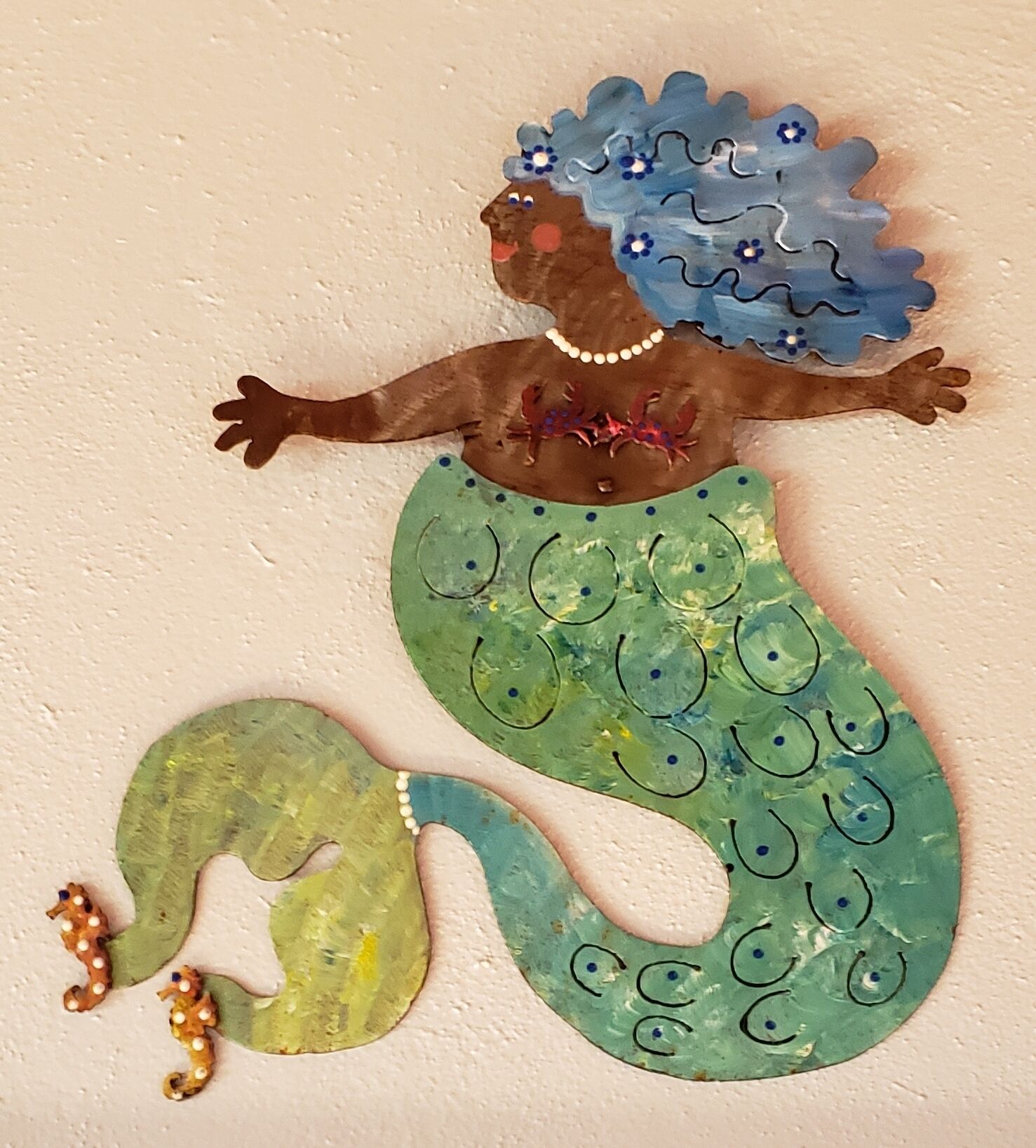 Een zeemeerminfiguur met een groene staart en blauw haar, bestaande uit losse puzzelstukjes, voor een effen muur.