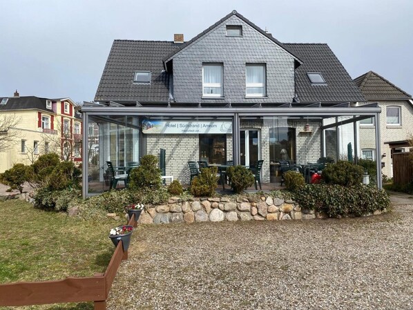 A hotel with a modern glass facade, a stone foundation, and a gravel driveway.