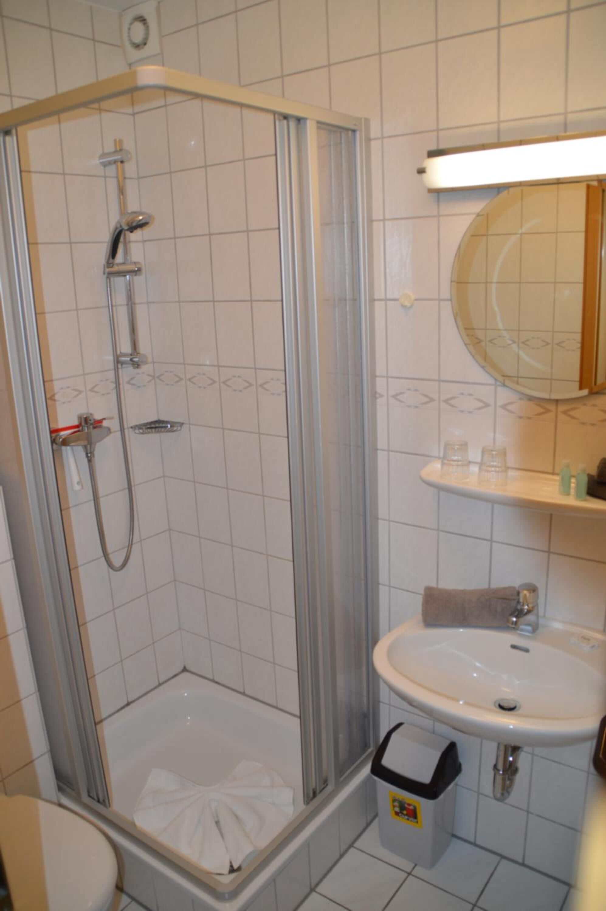 Et badeværelse med en brusekabine med glasvægge, en hvid vask og et spejl over vasken.