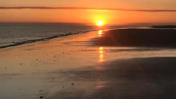 A beach at sunset with the sun low on the horizon, reflecting on the wet sand.