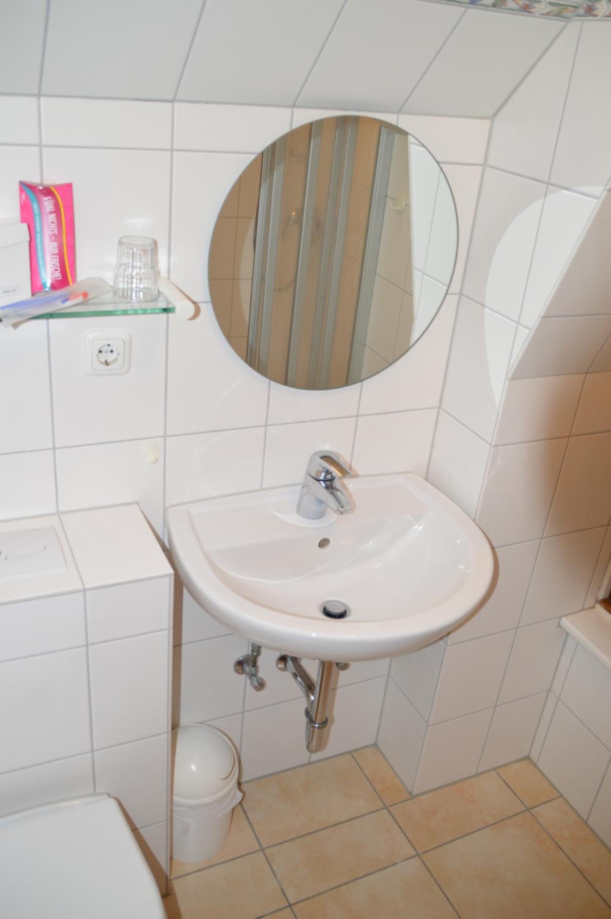 Un baño con lavamanos blanco, espejo y paredes de azulejos.