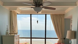 Ein Schlafzimmer mit einem Bett, einem Schminktisch, einem Sessel, einer Lampe und Blick auf den Ozean.
