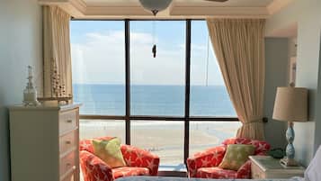 A bedroom with a bed, a dresser, a chair, a lamp, and a view of the ocean.