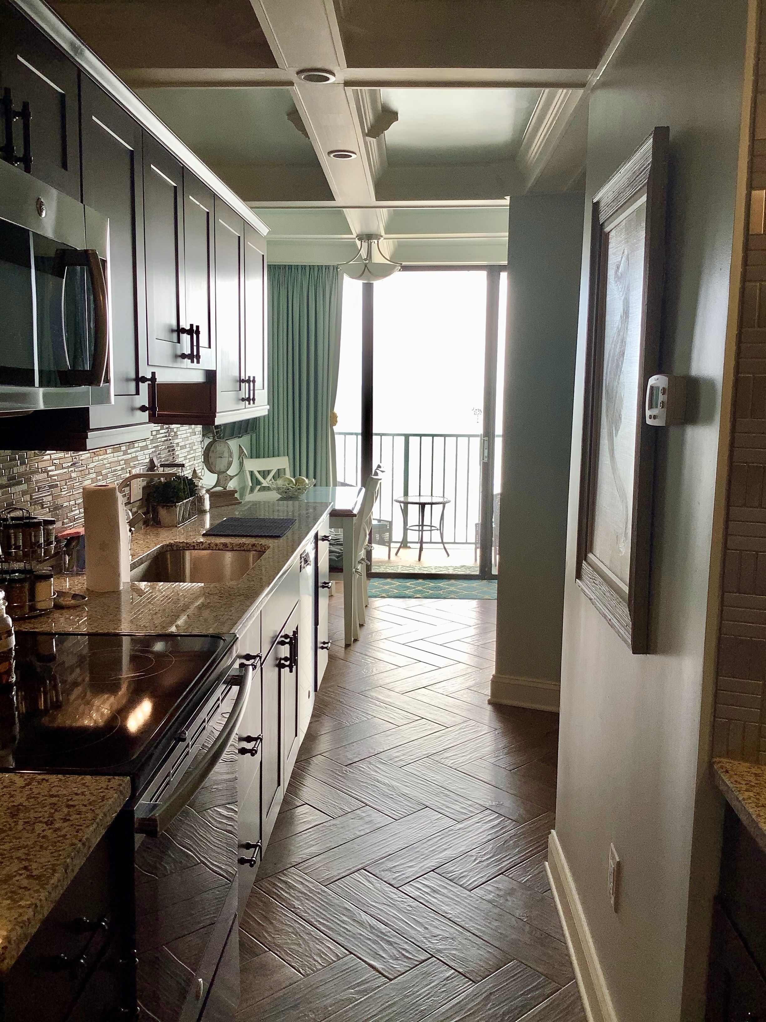 A kitchen with a herringbone floor, a large island with a microwave, and a view to a balcony.
