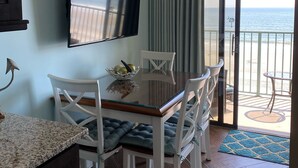 Ein Essbereich mit an der Wand montiertem Fernseher, einem Tisch mit Stühlen und Blick auf den Ozean durch eine Schiebetür.