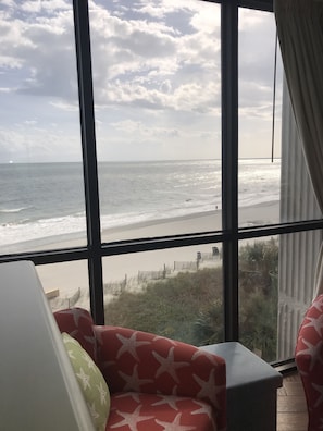 A room with a large window overlooking a beach. There is a red sofa with a star pattern and a green pillow. - Starfish Bay- Romantic Oceanfront couples suite- NEW LISTING (Myrtle Beach)