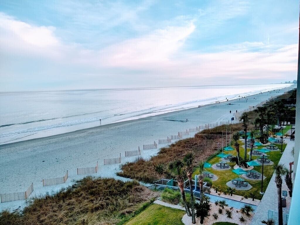 A beach view with a pathway leading to outdoor seating areas.