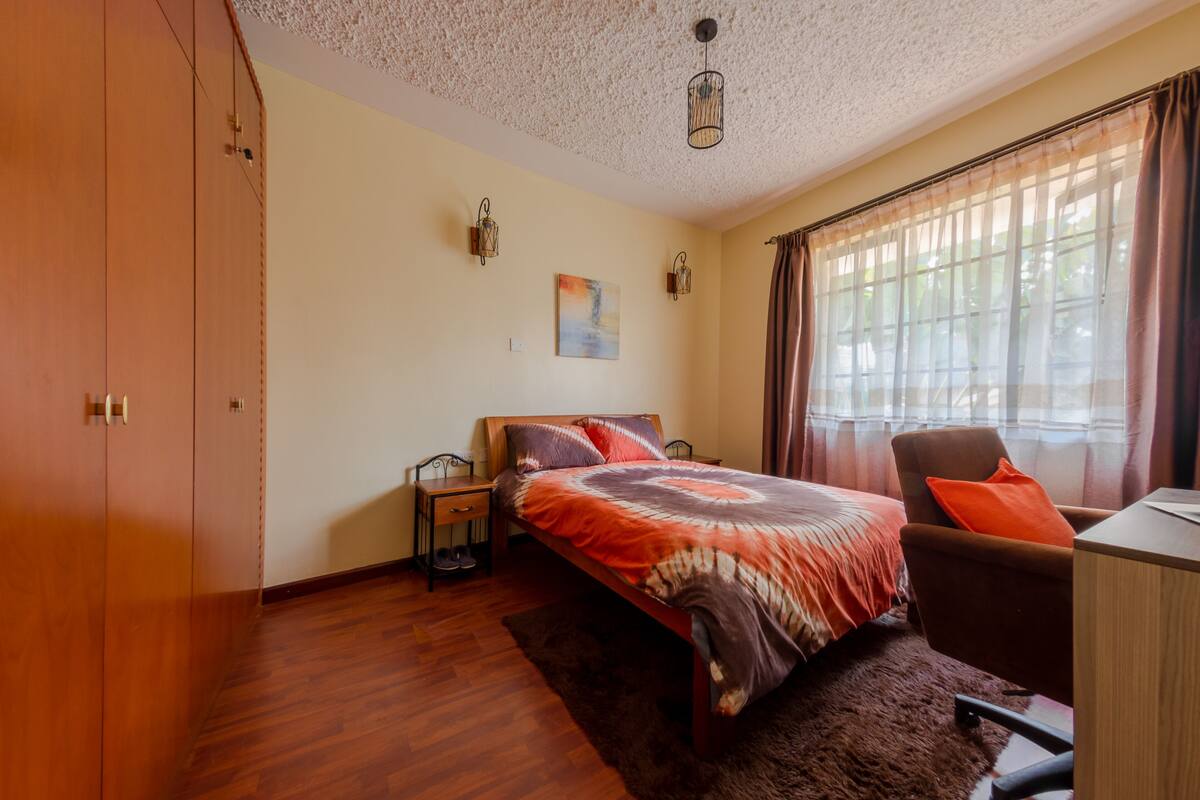 A bedroom with a bed, a desk, a chair, a wardrobe, and a painting on the wall.
