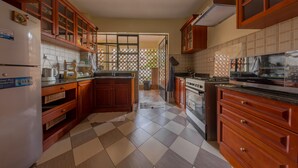 Une cuisine avec des meubles de rangement en bois, un réfrigérateur, une cuisinière et un sol carrelé.