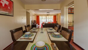 Une salle à manger avec une longue table dressée pour six personnes, entourée de chaises, un globe terrestre accroché au mur et un lustre au-dessus.