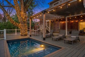 A poolside area with a wooden deck, lounge chairs, and a pergola with string lights. - Pool | Hot Tub | Covered Porch | Patio | Game Room (Lexington)