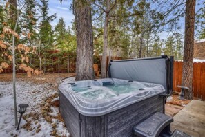 A hot tub in a wooded backyard with a wooden deck and a fence.
