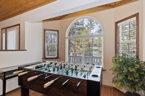 Una habitación con mesa de fútbol, ventanas amplias y una planta en maceta.