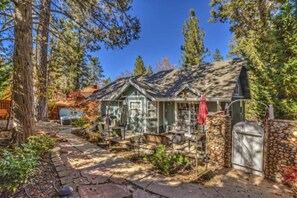 A rustic cabin with a stone wall and a wooden deck, surrounded by trees.