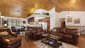 A spacious living area with leather sofas, a coffee table, and a dining area with a large window.