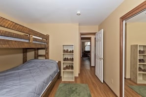 A bedroom with a bunk bed, a wooden wardrobe, and a hallway leading to a door.