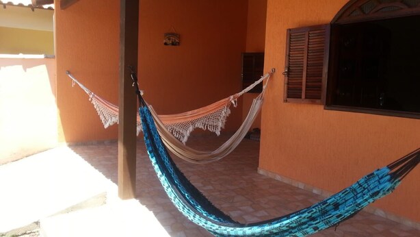 A hammock tied between two wooden posts in front of a building with orange walls and a tiled floor. - Casa de Praia Cordeirinho (Marica)