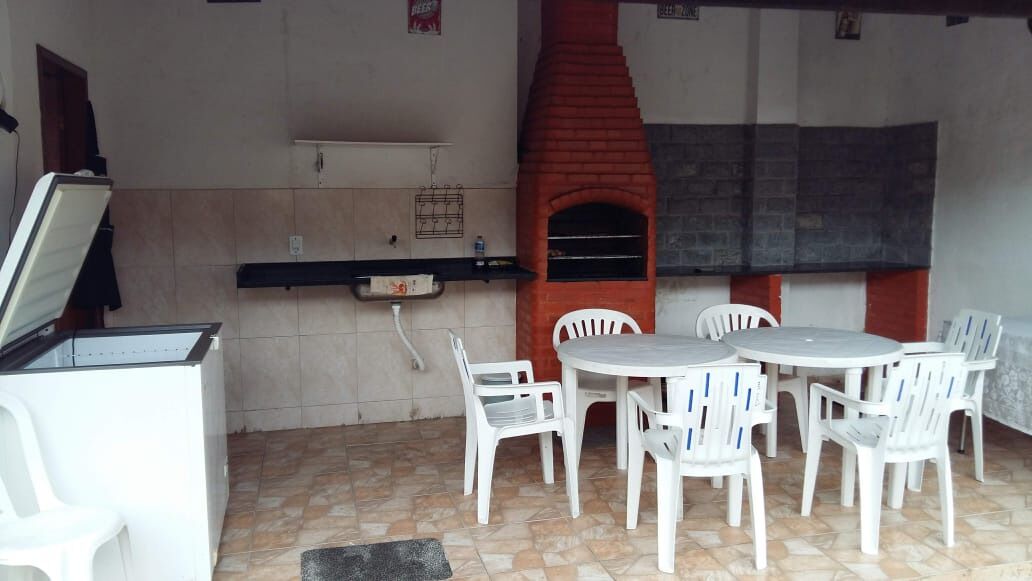 An outdoor patio with a brick oven, white plastic chairs, and a small table.