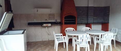 An outdoor patio with a brick oven, white plastic chairs, and a small table.