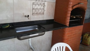 A kitchen with a black countertop, a sink, and a brick oven. - Casa de Praia Cordeirinho (Marica)