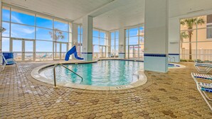 En indendørs swimmingpool med krystalklart havudsigt, flisegulv og liggestole.