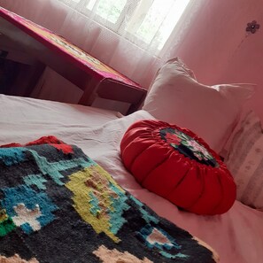 Cozy bedroom with a neatly made bed, featuring a white sheet and colorful blanket, and a decorative pillow.