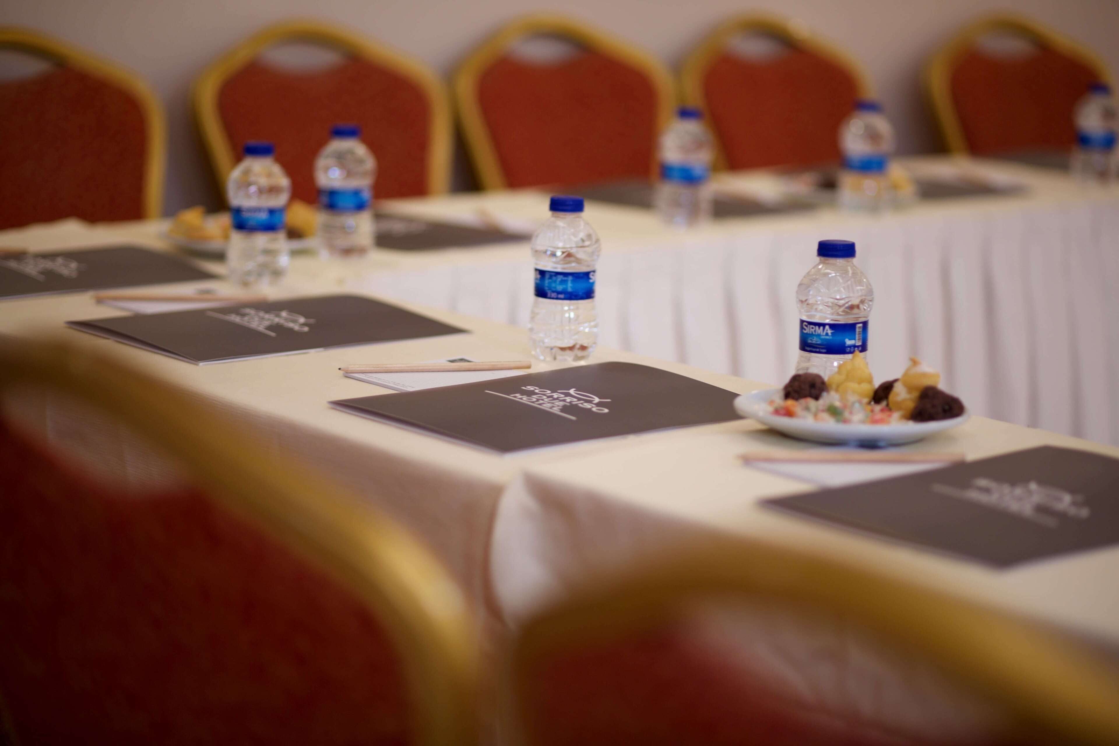 Une table de conférence avec des bouteilles d’eau, des porte-noms et une assiette de nourriture.