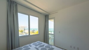 Une chambre d’hôtel dotée d’une grande fenêtre, d’un lit recouvert d’une couvre-lit à motifs géométriques et d’un balcon offrant une vue sur la plage.
