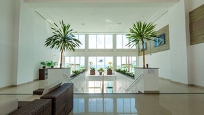 Un hall d’entrée spacieux avec un escalier central, des plantes en pot et une vue sur l’océan.