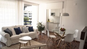 A modern living room with a sofa, coffee table, and chairs, a dining area with a glass table and chairs, and a kitchen with white cabinets and a microwave. - Comfortable apartment with pool and garden. (Torredembarra)
