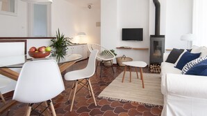 A modern living room with a sofa, chairs, a TV, a fireplace, and a dining area with a bowl of fruit. - Comfortable apartment with pool and garden. (Torredembarra)
