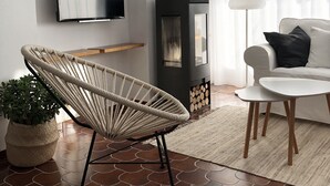 A modern living room with a flat-screen TV, a black wood-burning stove, a rattan chair, a white sofa, and a small wooden table. - Comfortable apartment with pool and garden. (Torredembarra)