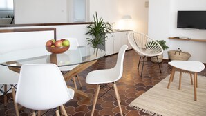 A modern kitchen with a glass dining table, white chairs, a bowl of fruit, and a hanging light fixture. - Comfortable apartment with pool and garden. (Torredembarra)