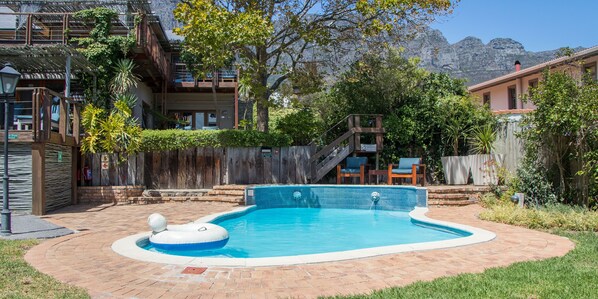 A swimming pool with a wooden deck, surrounded by a wooden fence and a mountain backdrop.