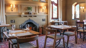 A dining area with wooden tables and chairs, a brick fireplace, and wall-mounted lamps.