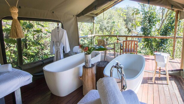 A spacious outdoor deck with a large bathtub, a wooden chair, and a hanging towel.