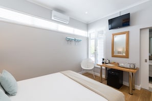 A modern hotel room with a bed, a desk, a chair, a TV, and a window with blinds.