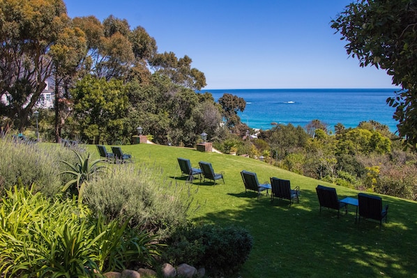 A grassy outdoor area with several chairs and a table, overlooking a body of water.