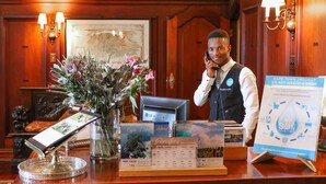 A hotel reception desk with a computer, a vase with flowers, informational brochures, and a water conservation sign.