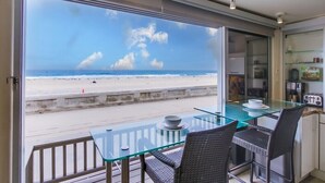 Ein Balkon mit Glastisch und Korbstühlen mit Blick auf einen Strand.