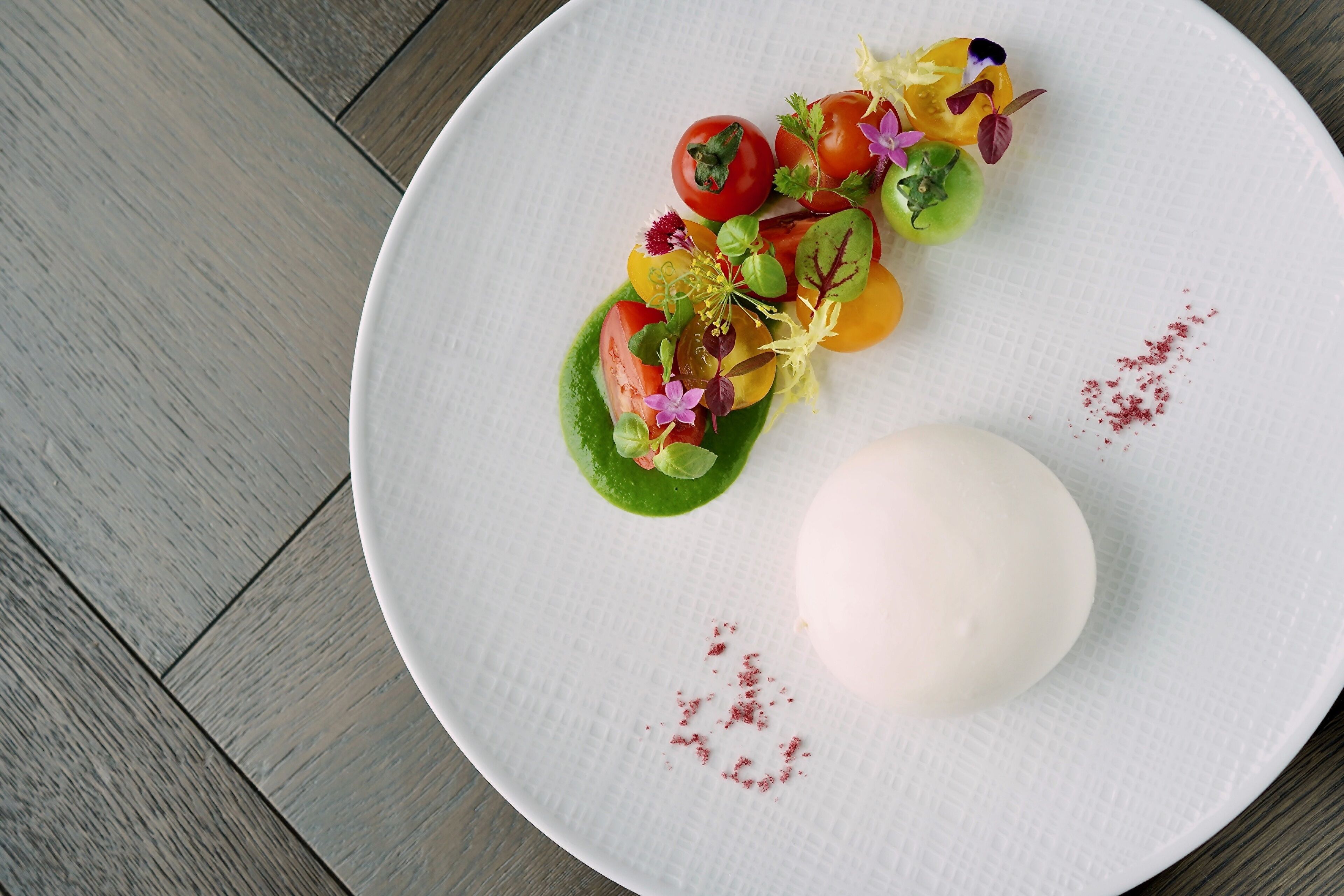 A white plate with a variety of colorful vegetables and a large white egg on a textured surface.