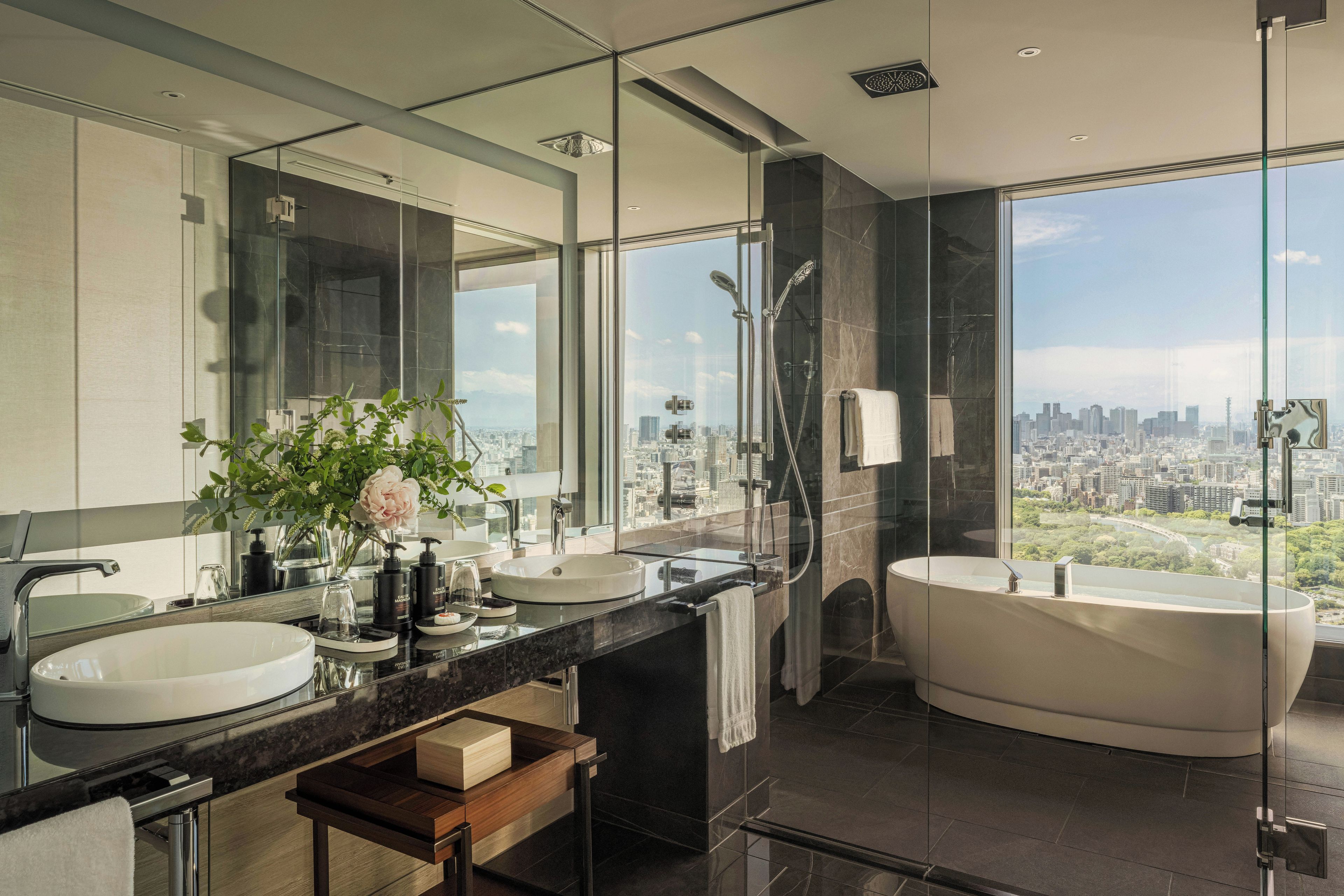 A modern bathroom with a large bathtub, two sinks, a vanity, and a city view.