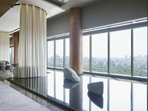 A modern hotel lobby with large windows, a high ceiling, and a view of a cityscape.