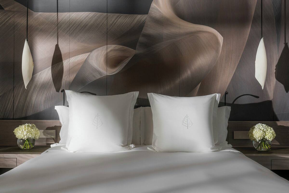 A modern hotel room with a large abstract painting on the wall, a neatly made bed with white linens, and two bedside tables with vases of flowers.