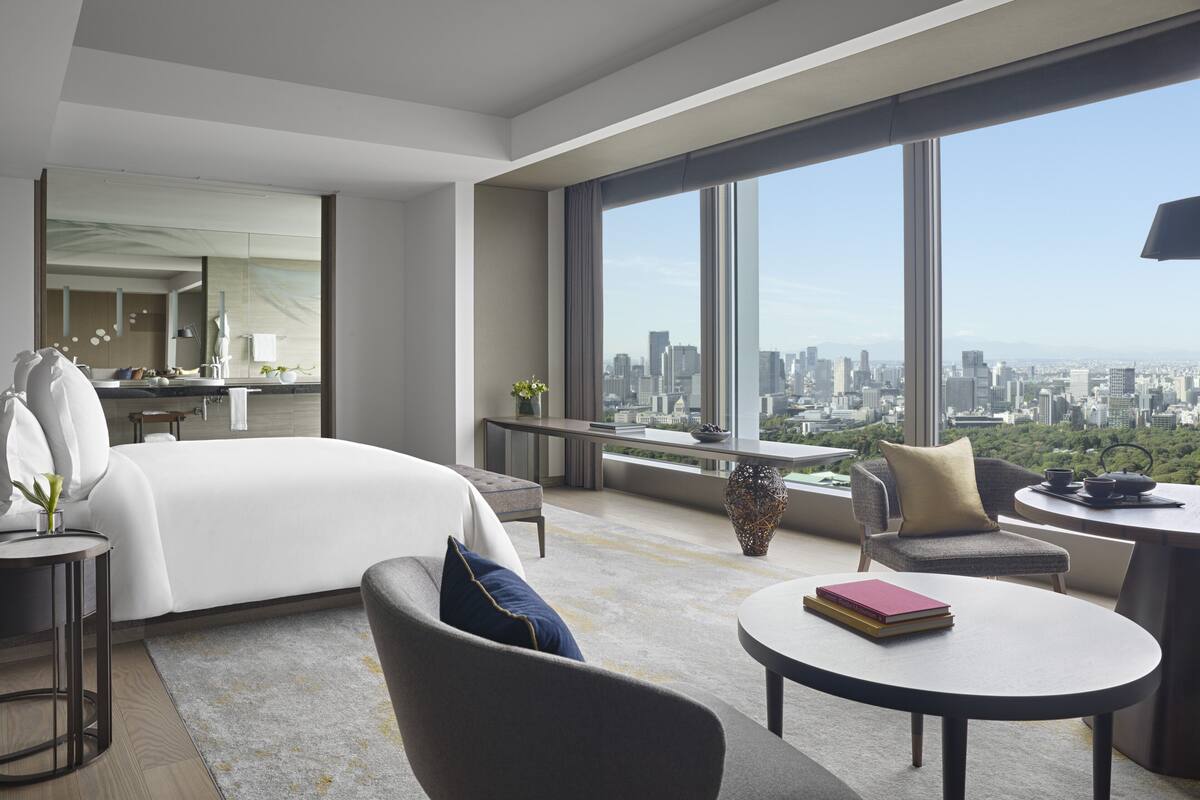 A modern hotel room with a large bed, a sitting area, and a city view.
