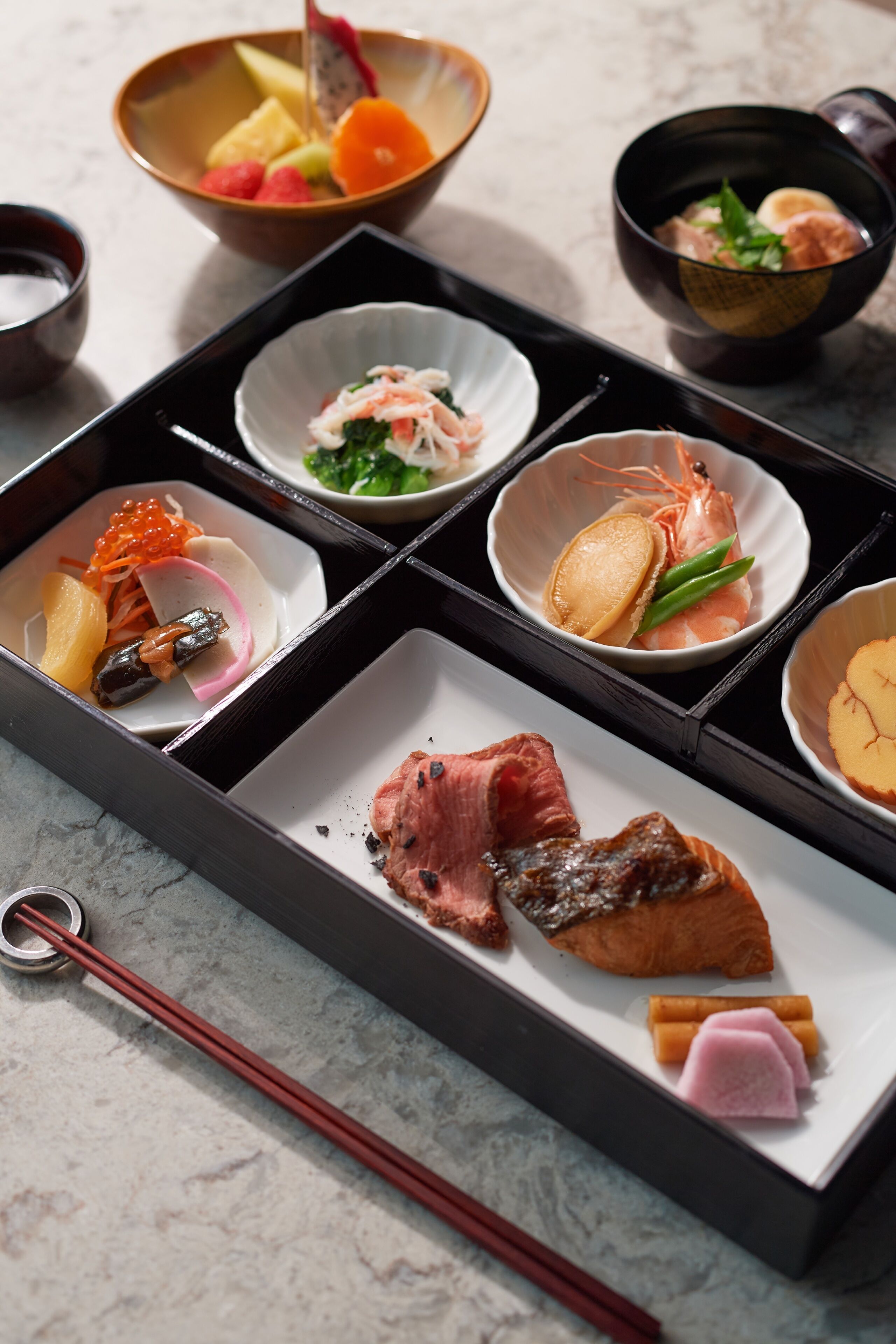 A traditional Japanese meal set with various dishes including sashimi, vegetables, and meat, arranged on a black tray.