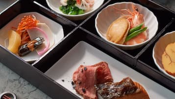 A traditional Japanese meal set with various dishes including sashimi, vegetables, and meat, arranged on a black tray.