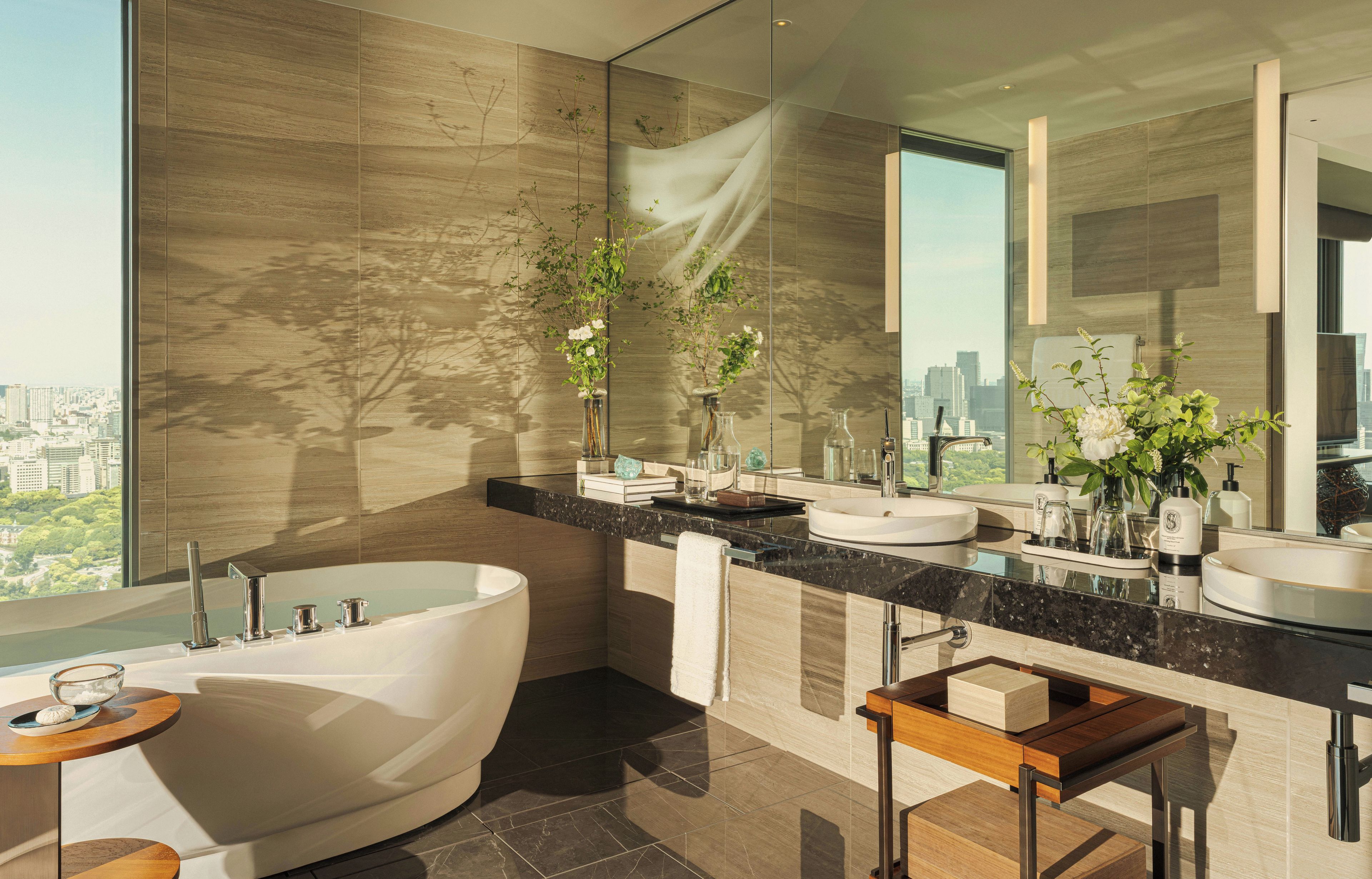 A modern bathroom with a freestanding bathtub, two sinks, and a large mirror reflecting the cityscape.